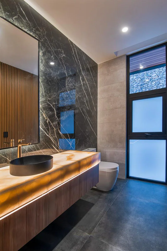 Baño de Cerro Alto 500 con piedra oscura, madera e iluminación integrada